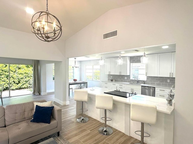 kitchen with a chandelier, a sink, stainless steel dishwasher, black electric stovetop, and high vaulted ceiling