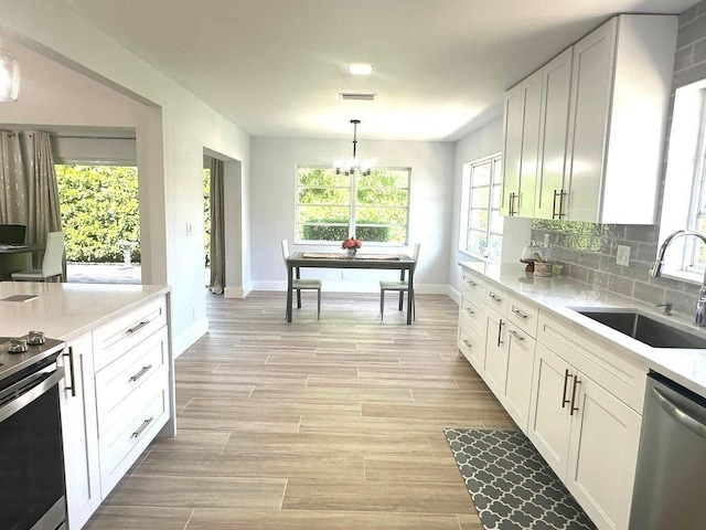 kitchen with a sink, appliances with stainless steel finishes, baseboards, white cabinets, and a chandelier
