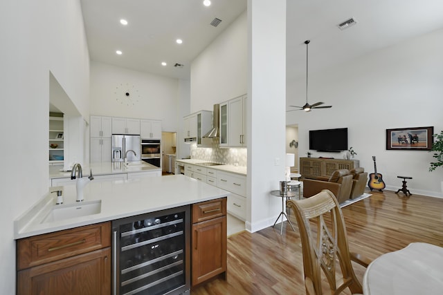 4054 SW Gleneagle Cir, Palm City, FL 34990 - bar area with beverage cooler, a sink, a towering ceiling, wall chimney exhaust hood, and light wood-style flooring