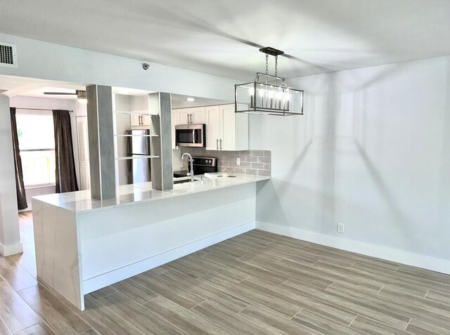 kitchen featuring stainless steel microwave, a peninsula, light wood-style flooring, baseboards, and white cabinets