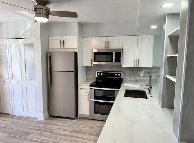 kitchen with stainless steel appliances, a sink, open shelves, light stone countertops, and white cabinetry