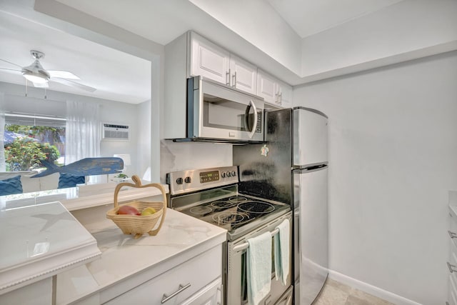 kitchen with appliances with stainless steel finishes, white cabinets, ceiling fan, an AC wall unit, and light stone counters