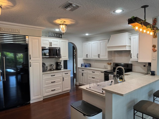 14324 Paddock Dr, Wellington, FL 33414 - kitchen with appliances with stainless steel finishes, custom range hood, arched walkways, a breakfast bar area, and a peninsula