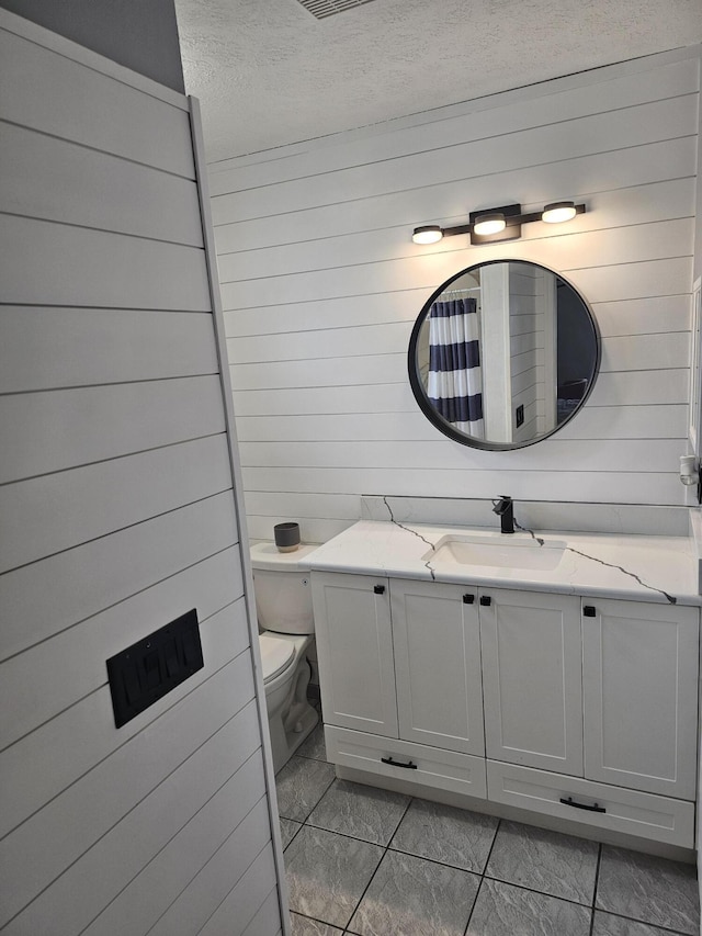 389 SE Whitmore Dr, Port Saint Lucie, FL 34984 - full bathroom featuring a textured ceiling, vanity, toilet, wood walls, and tile patterned flooring