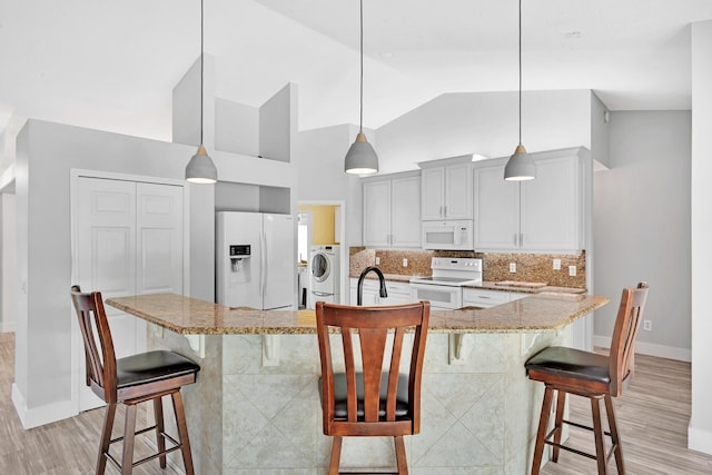 139 NE Royce Ave, Port Saint Lucie, FL 34983 - kitchen featuring white appliances, washer / clothes dryer, a kitchen bar, light wood-type flooring, and high vaulted ceiling