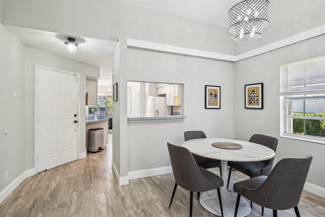 dining space with baseboards, light wood-style flooring, and a chandelier