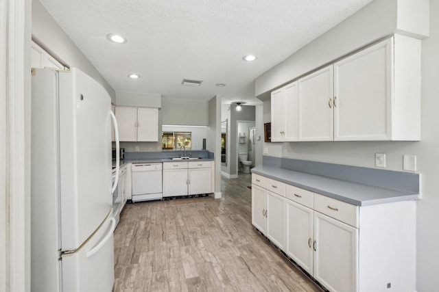 kitchen featuring white appliances, white cabinets, light wood finished floors, a sink, and recessed lighting
