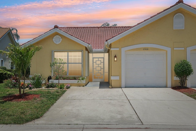 view of front of property with stucco siding, a tiled roof, driveway, and a garage