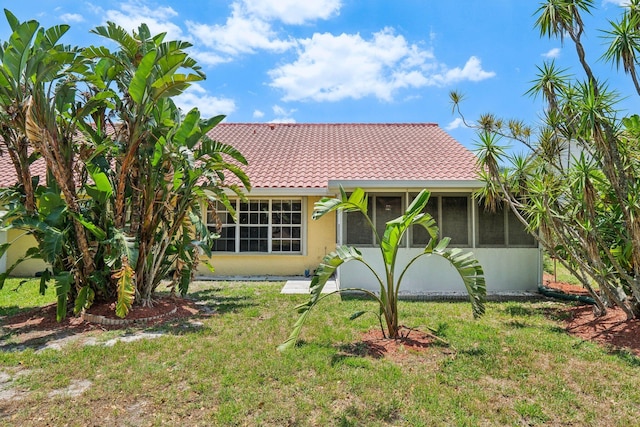 view of front of home featuring a sunroom, a front yard, a tile roof, and stucco siding
