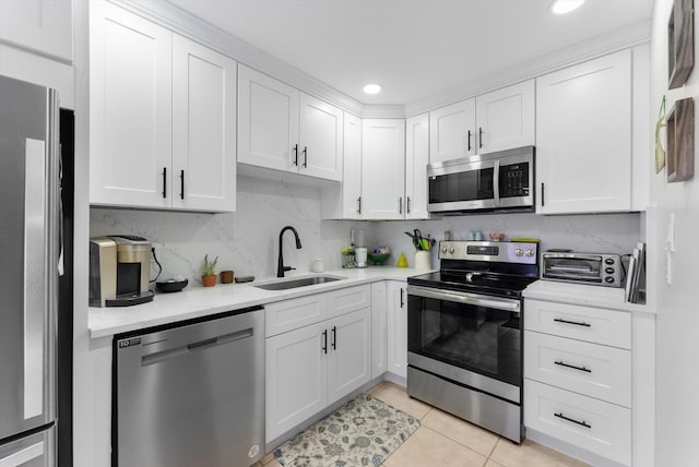 kitchen with appliances with stainless steel finishes, a sink, white cabinetry, light tile patterned flooring, and light countertops