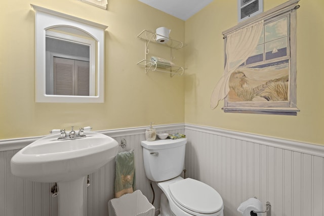 bathroom featuring a wainscoted wall, toilet, and a sink