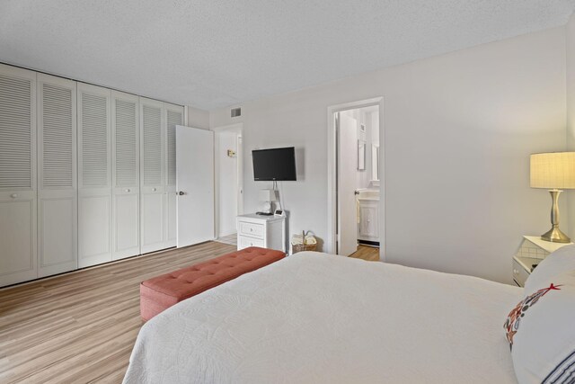 bedroom with wood finished floors, connected bathroom, a closet, and a textured ceiling