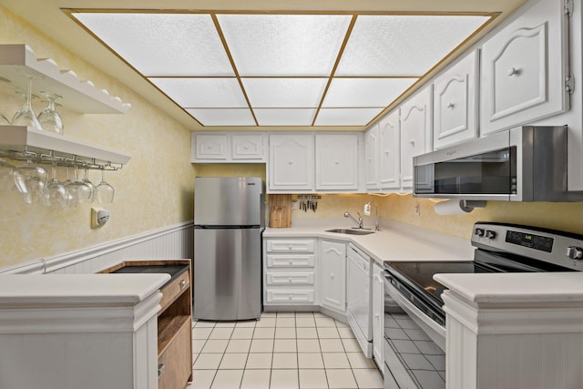 kitchen featuring stainless steel appliances, wainscoting, a sink, light tile patterned floors, and white cabinets