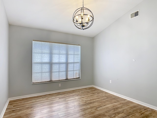 spare room with a chandelier, wood finished floors, and baseboards