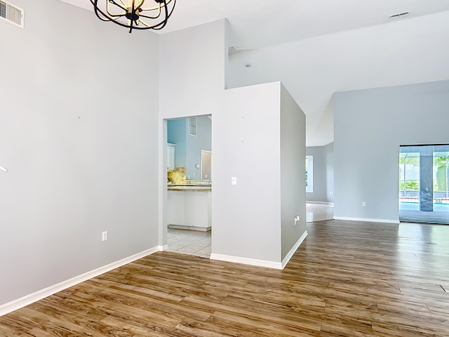 unfurnished room with high vaulted ceiling, light wood-style flooring, a chandelier, and baseboards