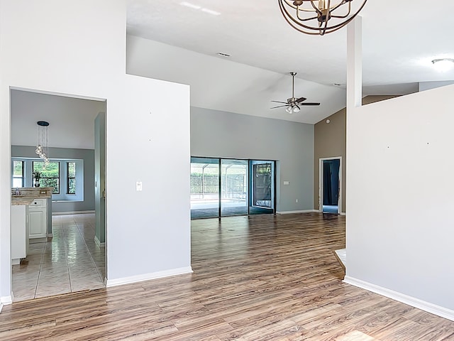 unfurnished room featuring high vaulted ceiling, light wood-style floors, a chandelier, baseboards, and a ceiling fan