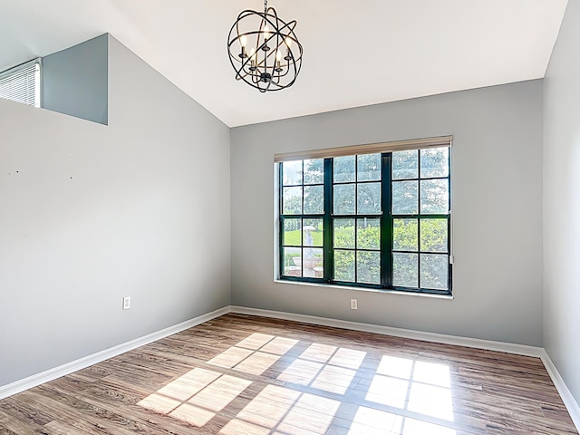 unfurnished room featuring a chandelier, vaulted ceiling, wood finished floors, and baseboards