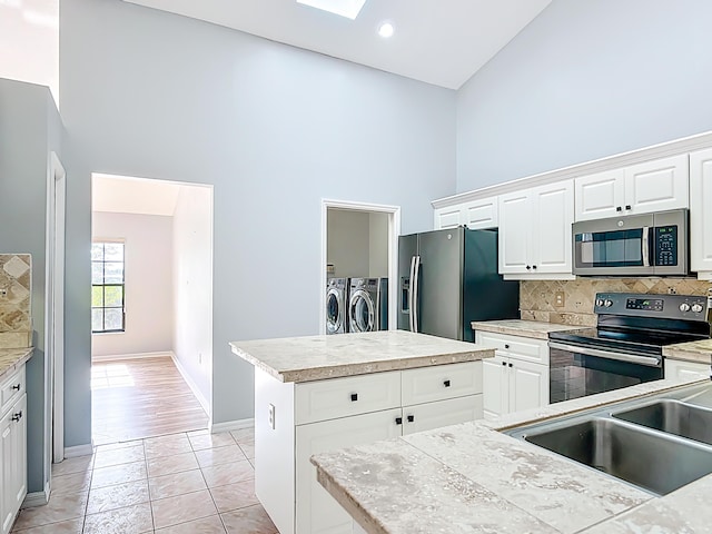 kitchen featuring stainless steel appliances, washing machine and dryer, a high ceiling, a kitchen island, and backsplash