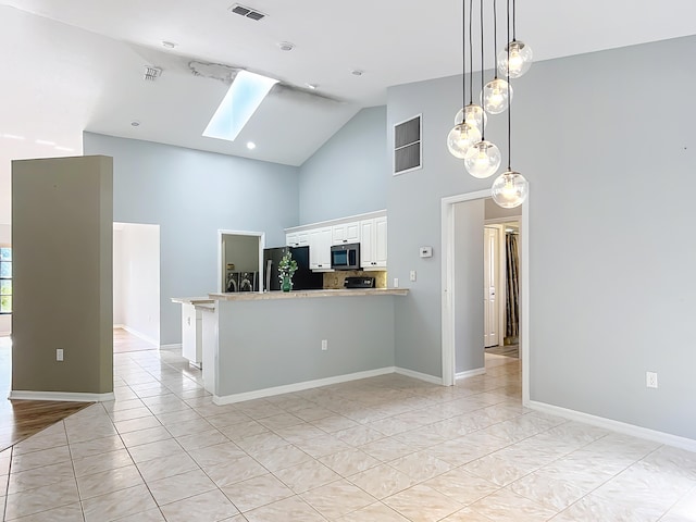 kitchen featuring black refrigerator, stainless steel microwave, a skylight, high vaulted ceiling, and white cabinetry