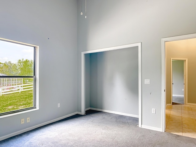 unfurnished room with carpet floors, baseboards, and a towering ceiling