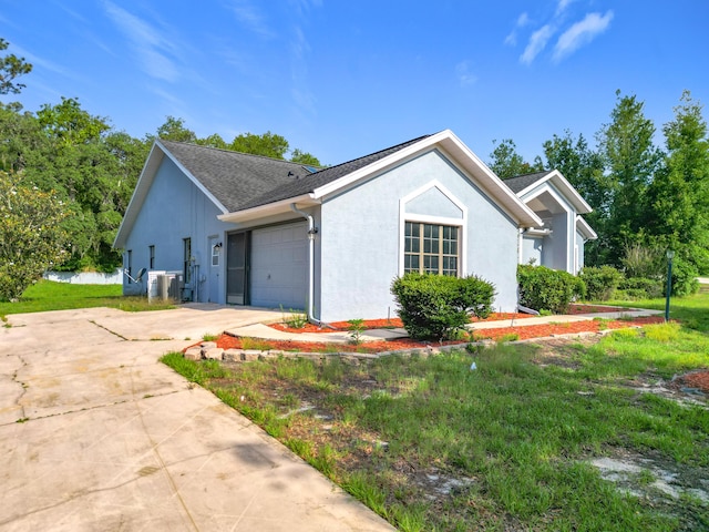 view of side of property featuring driveway, stucco siding, a garage, cooling unit, and roof with shingles