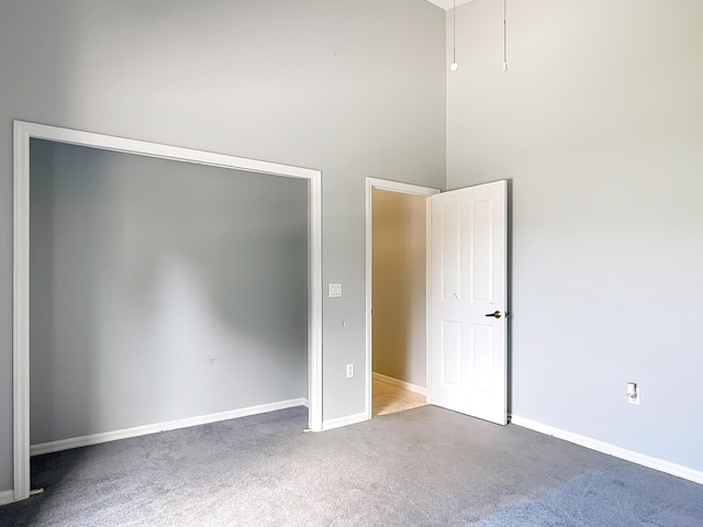 unfurnished bedroom featuring carpet flooring, baseboards, a towering ceiling, and attic access