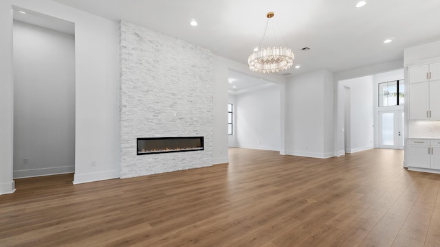 13250 Artisan Cir, Palm Beach Gardens, FL 33418 - unfurnished living room with a chandelier, light wood-style flooring, a stone fireplace, and recessed lighting
