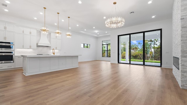 13250 Artisan Cir, Palm Beach Gardens, FL 33418 - unfurnished living room with a chandelier, light wood-type flooring, recessed lighting, and a fireplace