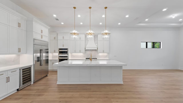 13250 Artisan Cir, Palm Beach Gardens, FL 33418 - kitchen with wine cooler, stainless steel appliances, custom range hood, light wood-type flooring, and white cabinetry