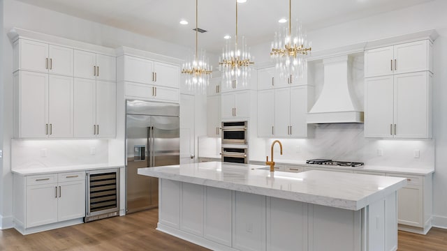 13250 Artisan Cir, Palm Beach Gardens, FL 33418 - kitchen with beverage cooler, appliances with stainless steel finishes, premium range hood, recessed lighting, and wood finished floors