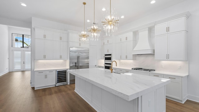 13250 Artisan Cir, Palm Beach Gardens, FL 33418 - kitchen with beverage cooler, custom range hood, appliances with stainless steel finishes, recessed lighting, and a chandelier