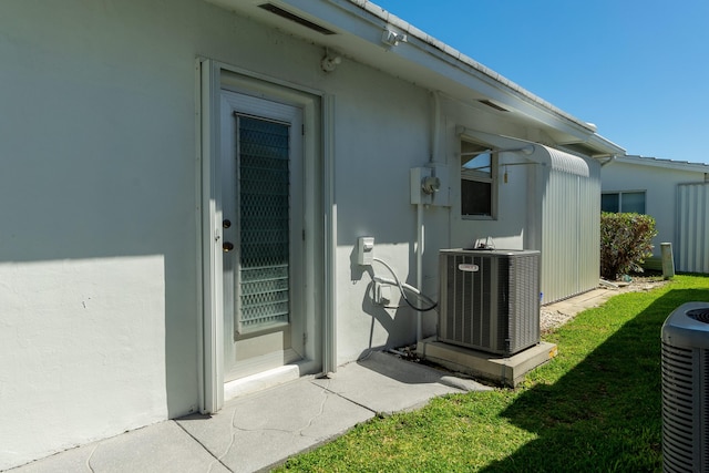 entrance to property featuring central AC unit, stucco siding, and a yard