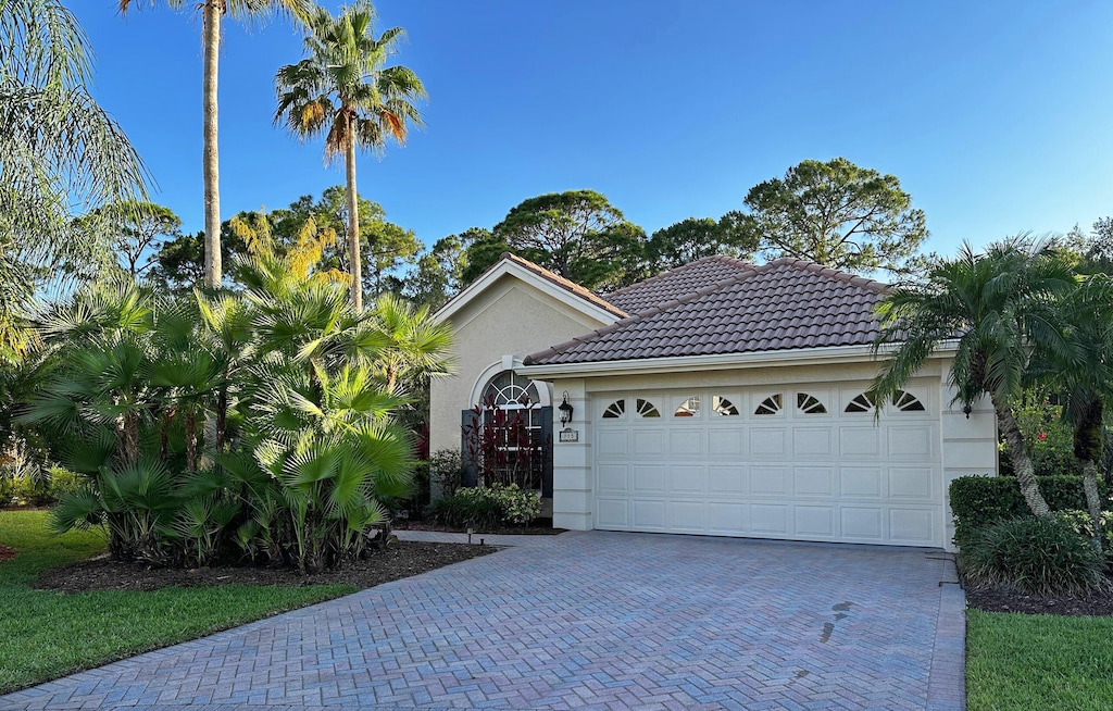 view of front facade with decorative driveway, a garage, stucco siding, and a tiled roof