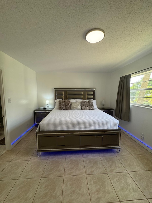 bedroom featuring a textured ceiling, light tile patterned floors, and baseboards