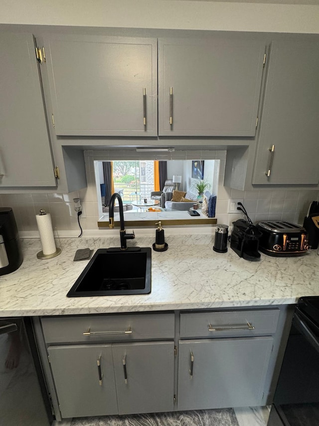 kitchen with gray cabinets, a sink, backsplash, and stove