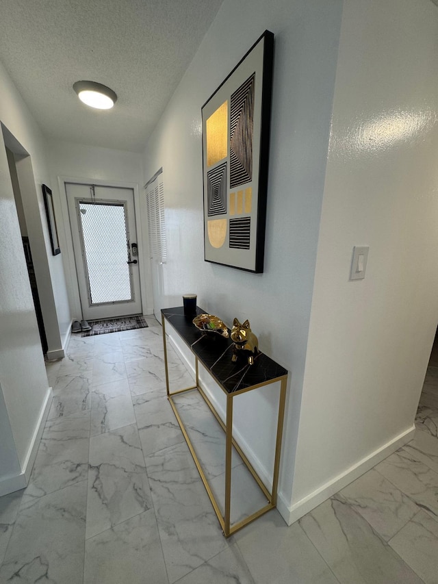 doorway with marble look tile flooring, baseboards, and a textured ceiling