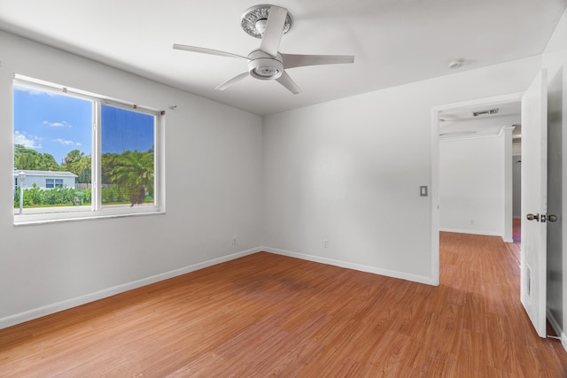 empty room featuring light wood-style flooring, a ceiling fan, a smoke detector, and baseboards
