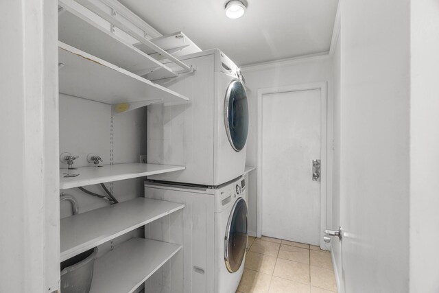 clothes washing area with stacked washer / drying machine, light tile patterned floors, and crown molding