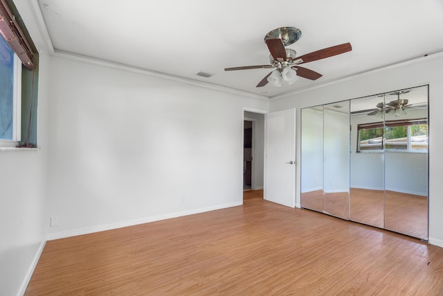 unfurnished bedroom featuring light wood-type flooring, crown molding, baseboards, ceiling fan, and a closet