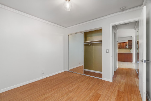 unfurnished bedroom with light wood-type flooring, a closet, baseboards, and ornamental molding