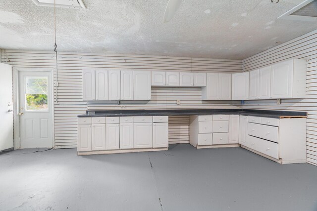 kitchen with concrete flooring, a textured ceiling, dark countertops, and white cabinetry