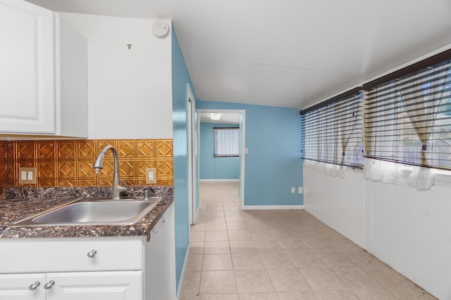 kitchen with a sink, dark countertops, light tile patterned flooring, white cabinetry, and tasteful backsplash