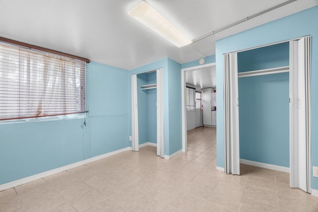 unfurnished bedroom featuring two closets, light tile patterned flooring, and baseboards