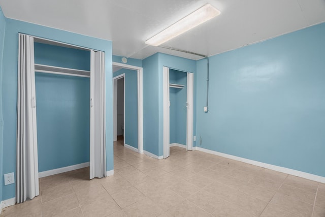 unfurnished bedroom with multiple closets, light tile patterned floors, and baseboards