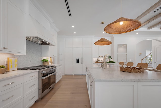 kitchen featuring high end stainless steel range, a sink, backsplash, arched walkways, and an island with sink