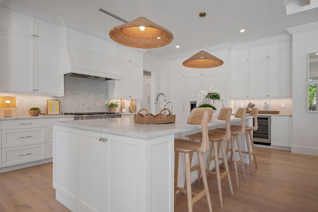 kitchen with beverage cooler, tasteful backsplash, light wood-style floors, white cabinetry, and ornamental molding
