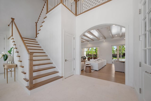 stairs featuring arched walkways, a high ceiling, wood finished floors, beam ceiling, and recessed lighting