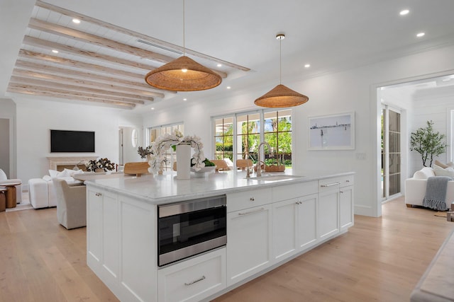 kitchen with a sink, open floor plan, stainless steel microwave, white cabinetry, and light wood-style floors
