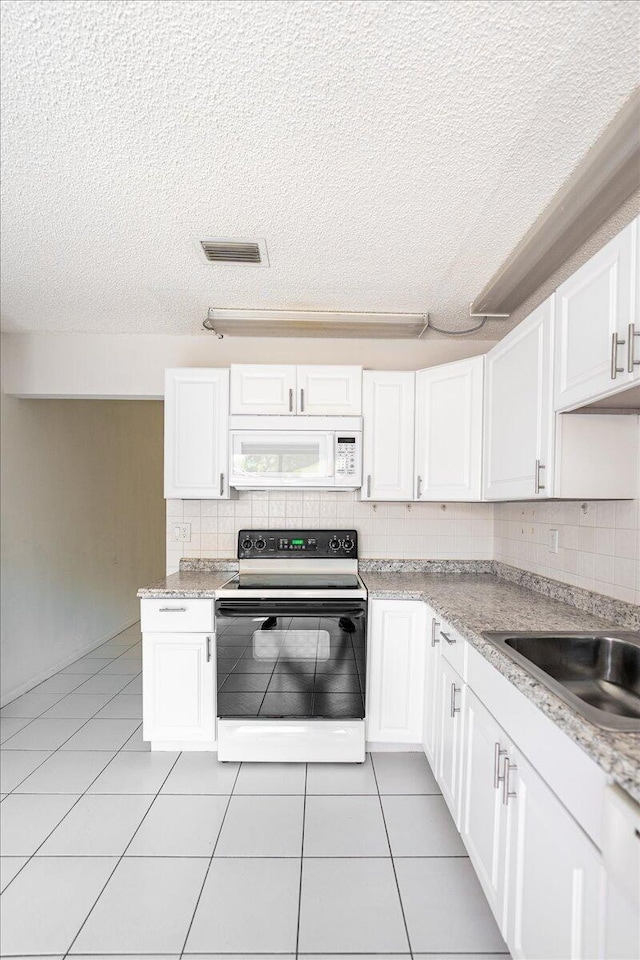 kitchen featuring electric stove, white microwave, a textured ceiling, decorative backsplash, and light countertops