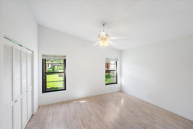 unfurnished bedroom with wood finished floors, lofted ceiling, a closet, a textured ceiling, and baseboards